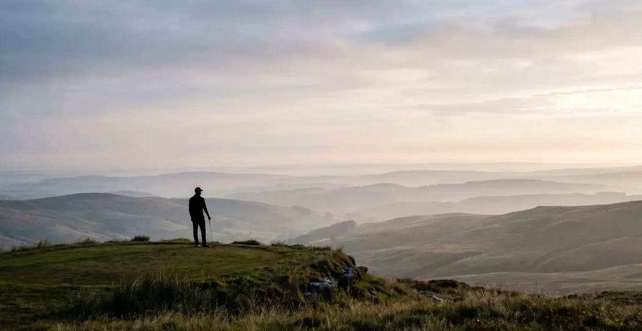 Golfer standing on elevated tee looking at distant horizon with expansive landscape view