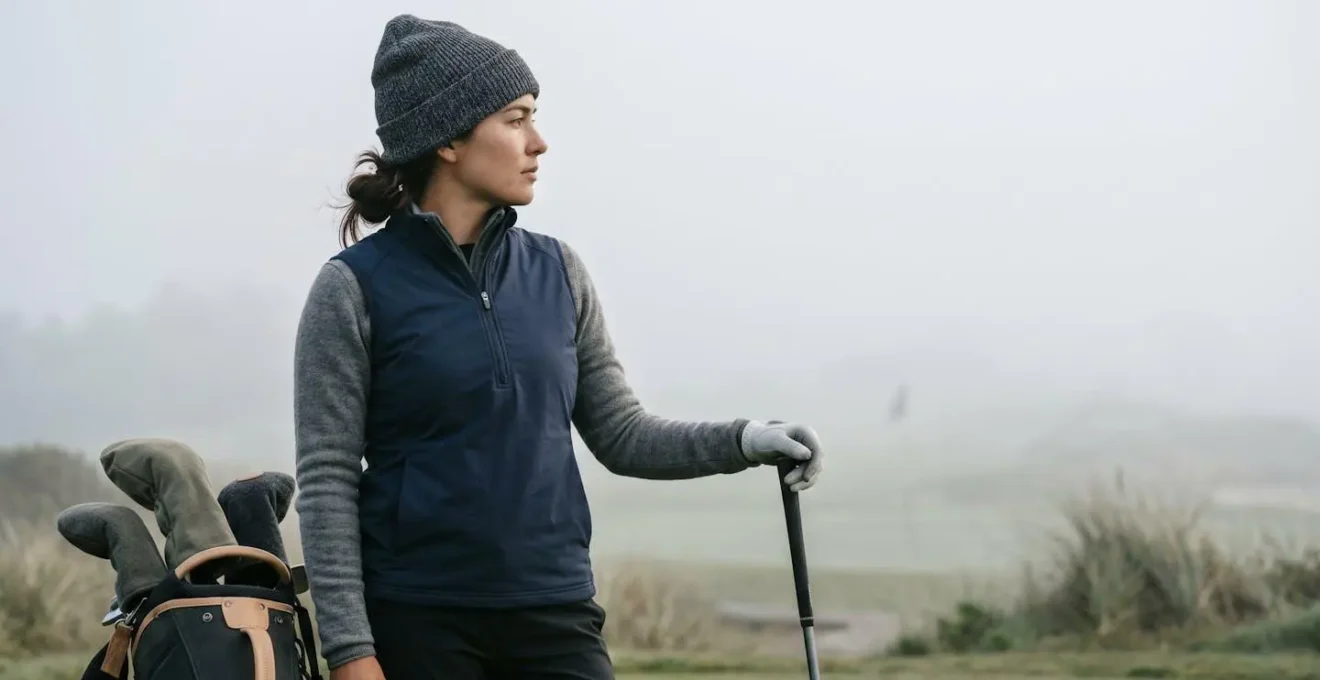 Golfer in layered clothing consulting smartphone for weather data on foggy coastal first tee