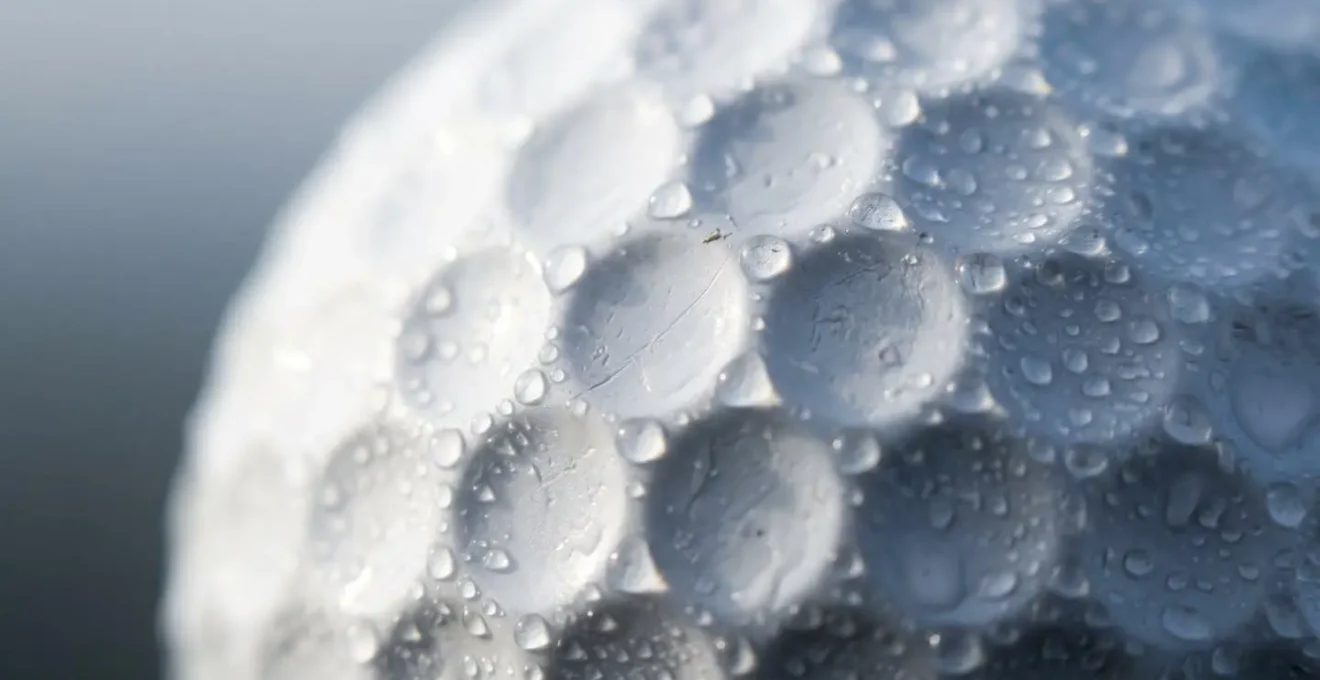 Extreme close-up of golf ball dimples with morning dew condensation illustrating air density effects