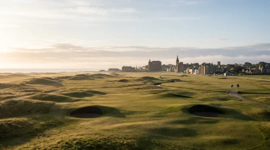 Wide angle view of the iconic Old Course at St Andrews with morning light casting shadows across undulating fairways