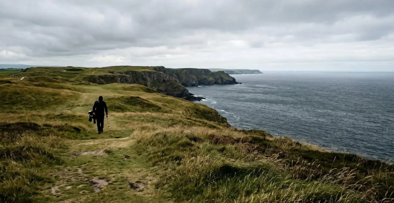 Golfer walking scenic coastal links course with panoramic ocean views and dramatic elevation